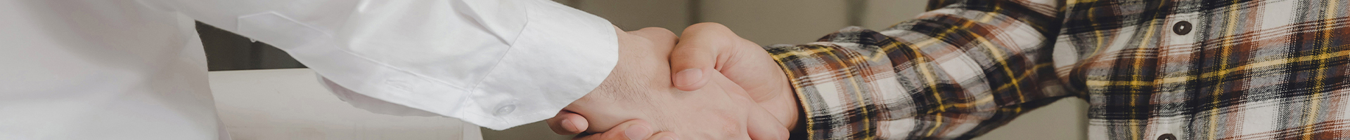 Close-up of two people shaking hands, one wearing a plaid shirt and the other a white sleeve.