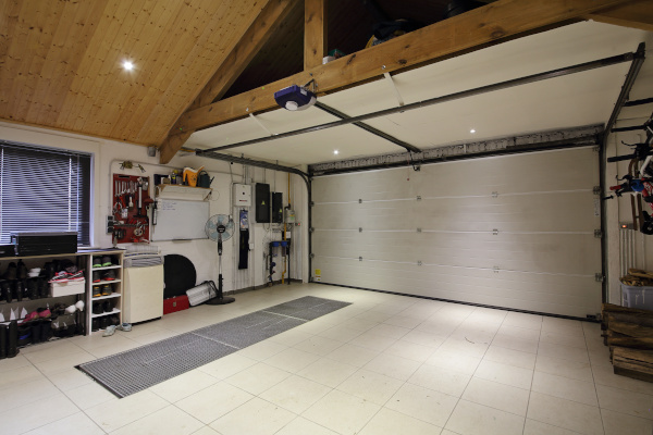 Clean, organized garage with tiled floors, a large closed door, and a workstation with tools and shelving along one wall.