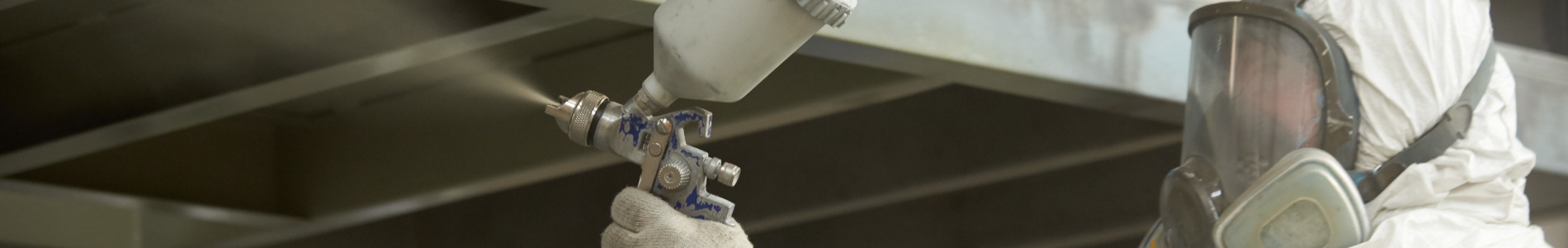 A man in a white uniform applies paint with a spray gun on a metal product.