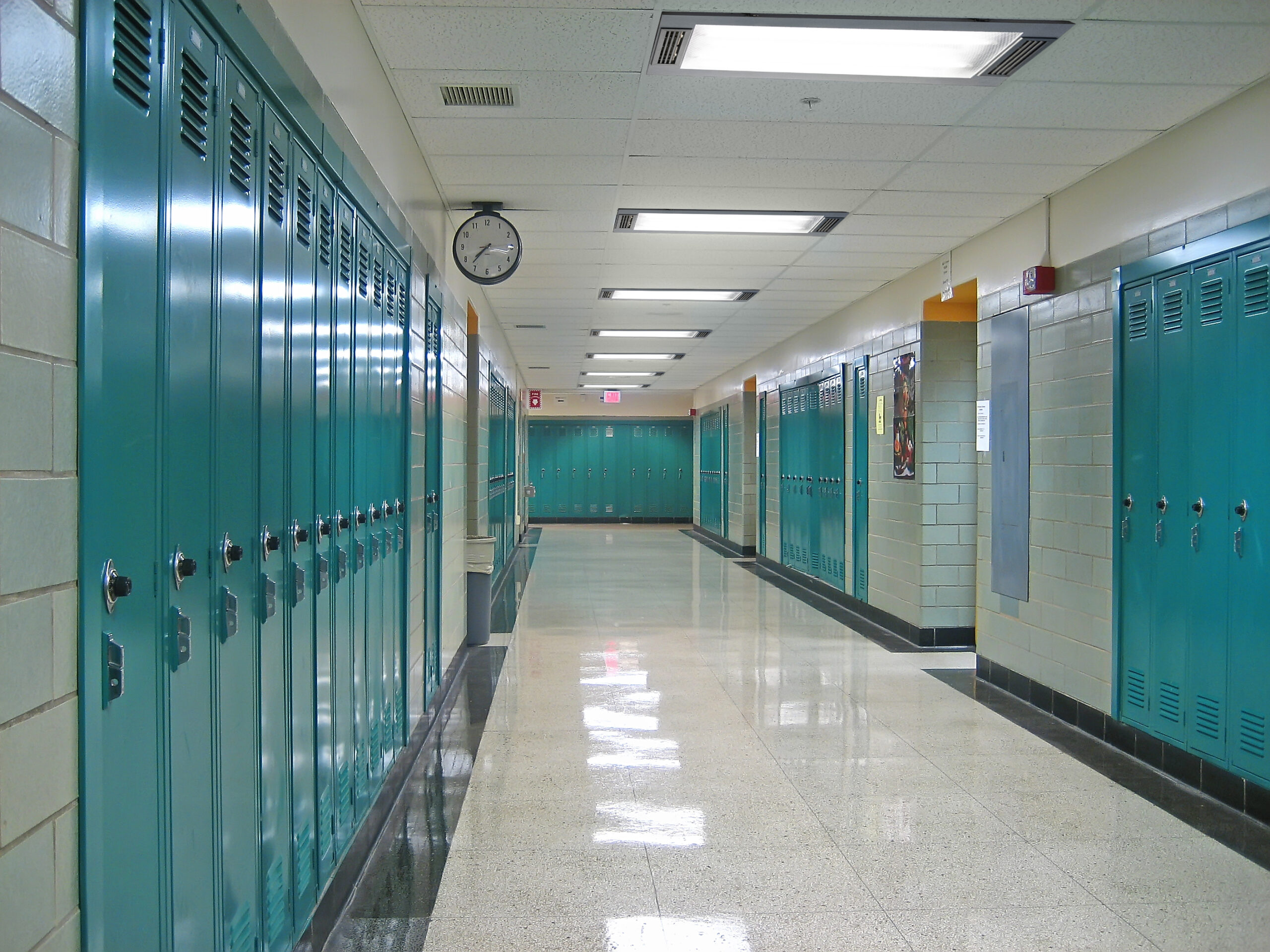 long school hallway with brick walls, polished white and gray tile floor, and blue full-length lockers