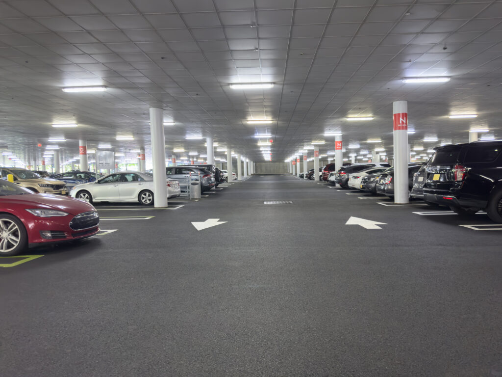 A spacious, well-lit indoor parking garage with cars neatly parked on both sides and directional arrows on the asphalt.