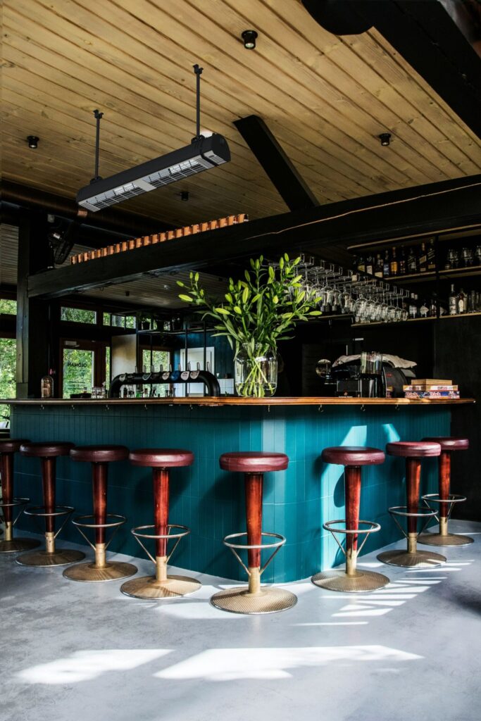 A semi-enclosed restaurant and bar with brown and gold bar stools, bar, and MEQ infrared heater with wooden rood.