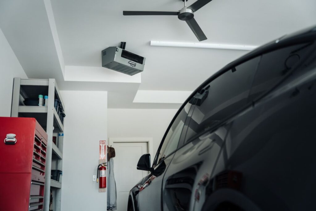 Modern garage interior with a parked black car, wall shelving, a red tool chest, and a ceiling-mounted Modine heating unit.