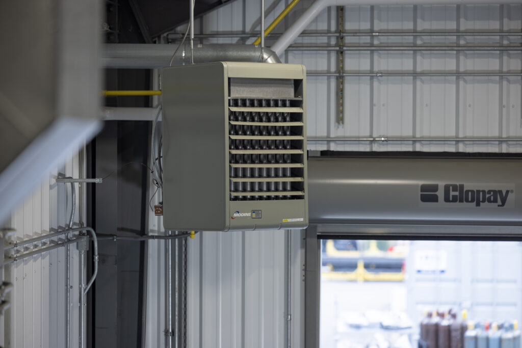 modine gas-fired power-vented unit heater, model PDP, ceiling mounted in an industrial garage with large bay door in the background