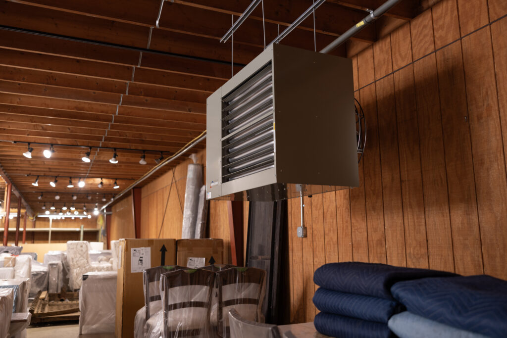 Modine power-vented gas-fired horizontal commercial unit heater, model PTP, installed in a commercial storage room with wood panel walls, filled with furniture wrapped and packaged for shipping.