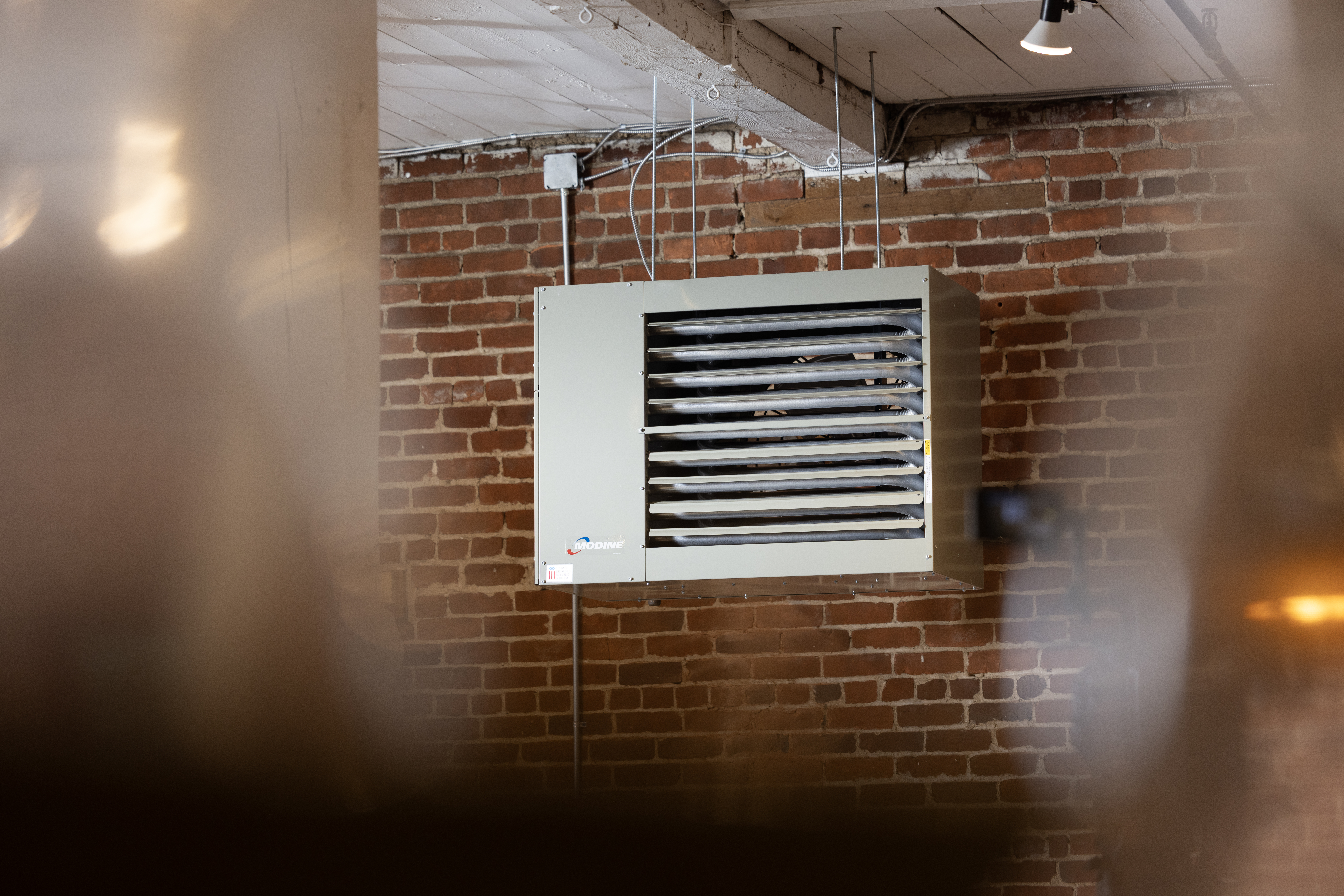 Modine commercial gas-fired power-vented unit heater, model PTP, mounted on the ceiling of a historic building's storage room with brick walls and a wooden roof.